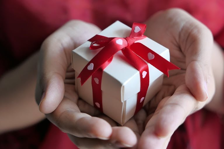 A heartfelt moment captured with hands holding a small gift box tied with a red ribbon.